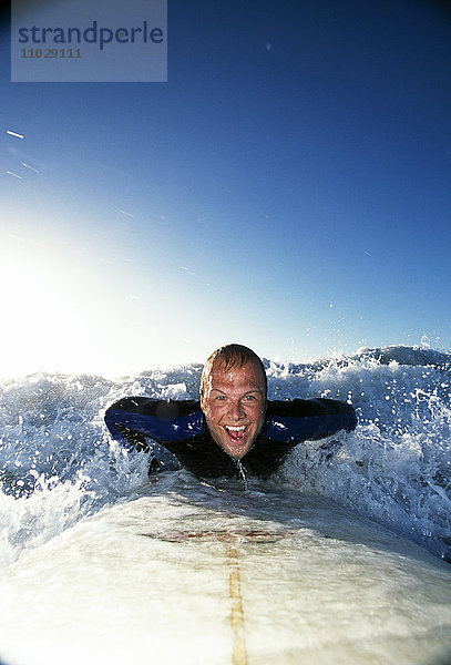 Mann auf Surfbrett in den Wellen liegend.