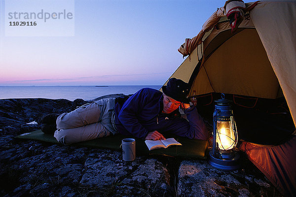 Ein Mann liest vor einem Zelt.