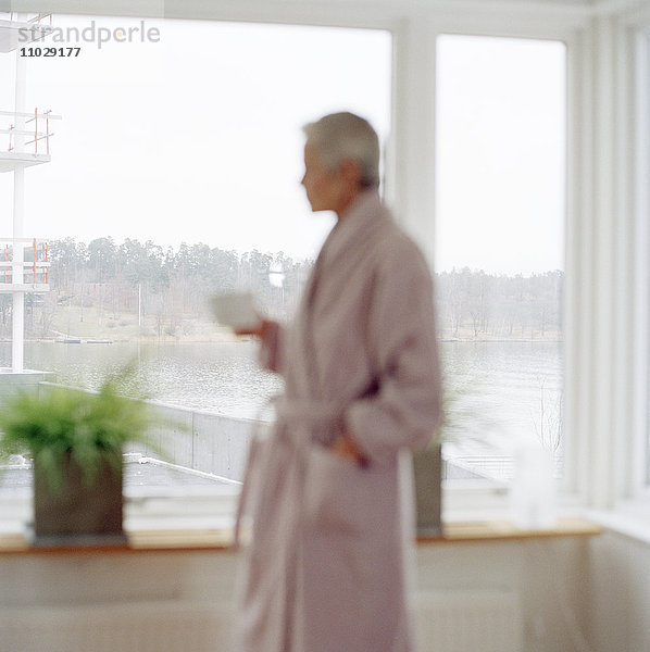 Eine Frau im Morgenmantel an einem Fenster.
