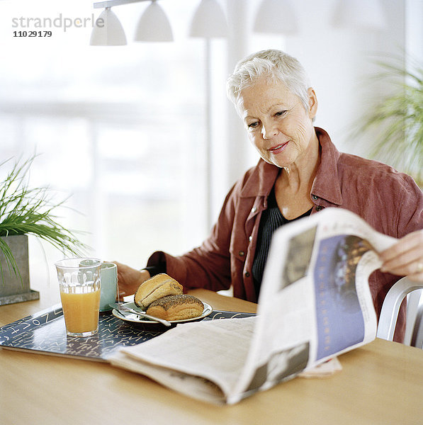 Eine Frau frühstückt und liest eine Zeitung.