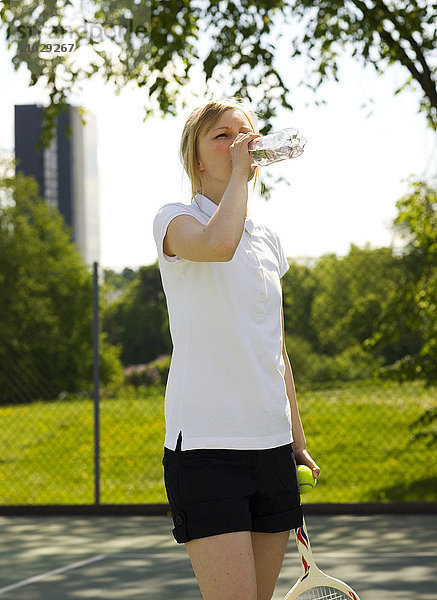 Junge Frau hält Tennisschläger und trinkt Wasser