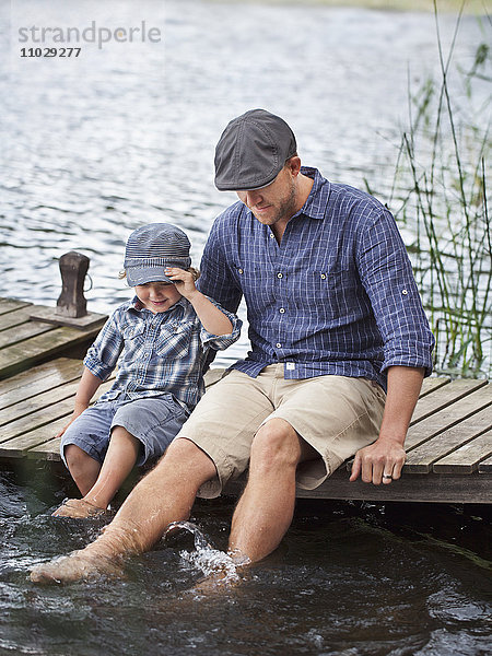 Mann mit Sohn sitzt auf dem Steg am See