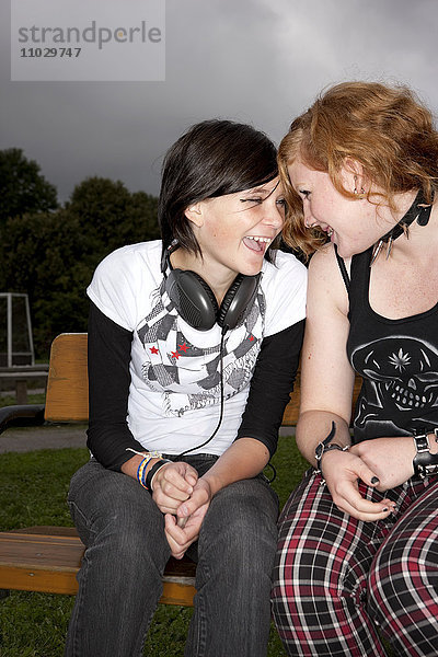 Zwei Mädchen im Teenageralter lachen auf einer Parkbank