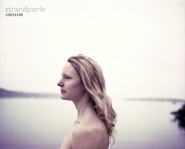 Nackte junge Frau mit Blick aufs Meer  Schweden
