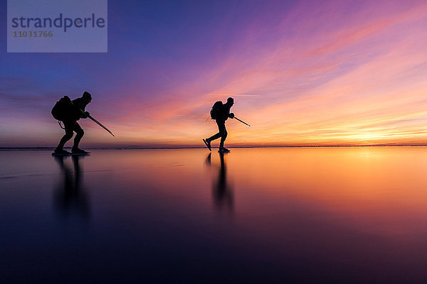 Menschen beim Schlittschuhlaufen bei Sonnenuntergang  Vanern  Schweden