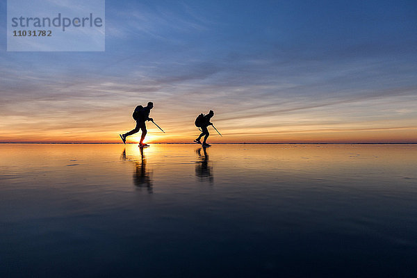 Menschen beim Schlittschuhlaufen bei Sonnenuntergang  Vanern  Schweden