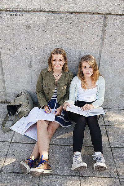 Zwei Teenager-Mädchen sitzen auf dem Bürgersteig