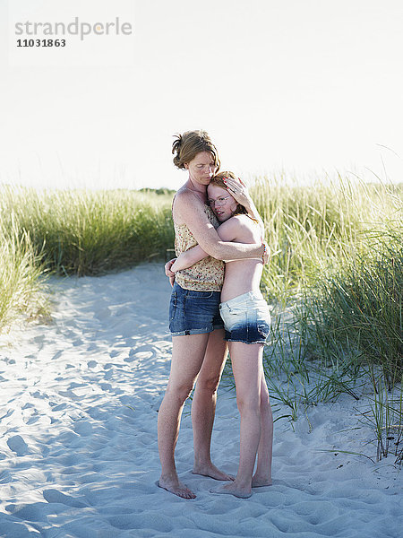 Mutter umarmt jugendliche Tochter am Strand