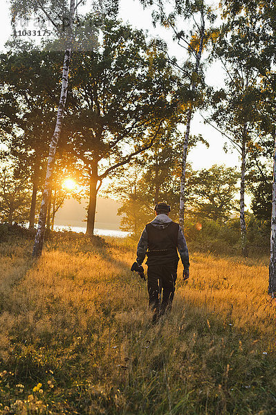 Jäger geht bei Sonnenuntergang durch ein Feld