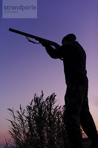 Jäger hält Gewehr am See in der Abenddämmerung