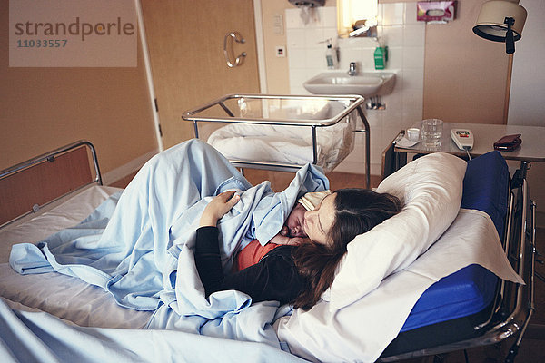 Schlafende Mutter mit neugeborenem Baby im Krankenhausbett