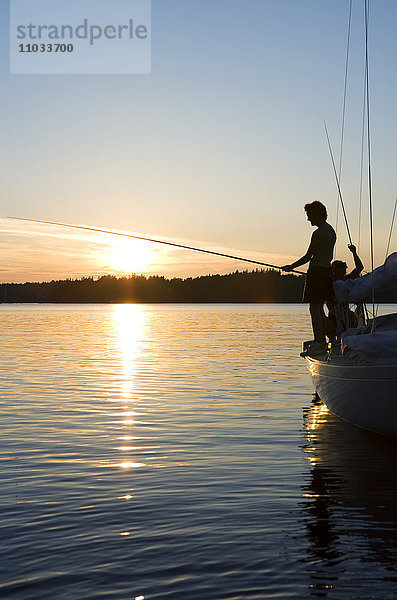 Zwei Männer fischen von einem Segelboot aus im Sonnenuntergang.