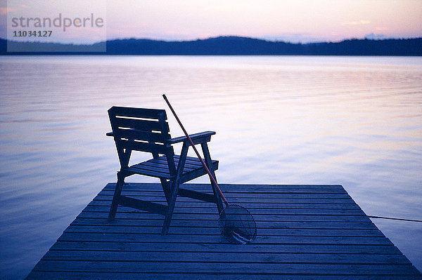 Ein Fischernetz  das bei Sonnenuntergang an einem Stuhl auf einem Pier lehnt.