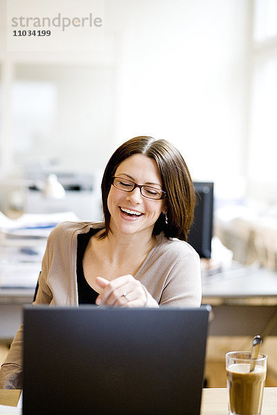 Eine lachende Frau an ihrem Arbeitsplatz.