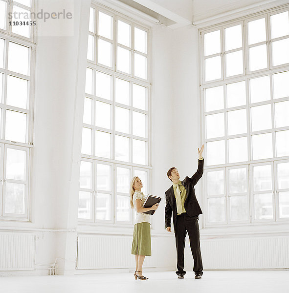Ein Mann und eine Frau in einem großen leeren Raum mit Fenstern.