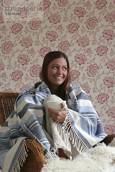 Skandinavische Frau mit einer Tasse Kaffee  die sich eine Decke um den Hals gelegt hat.