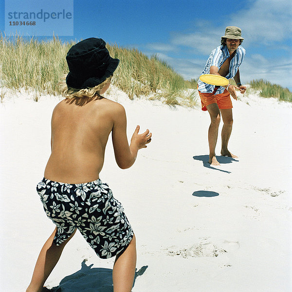 Vater und Sohn spielen mit einer Flugscheibe am Strand  Schweden.