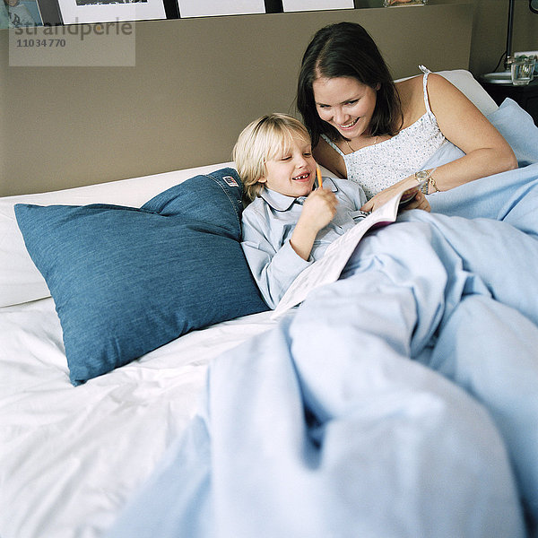 Mutter und Sohn liegen im Bett und lesen eine Zeitung  Hammarby Sjostad  Schweden.