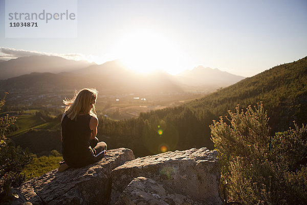 Frau sitzt auf einem Berg und betrachtet den Sonnenuntergang