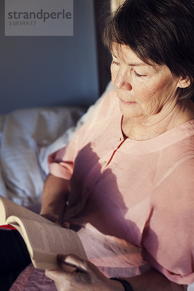 Ältere Frau liest Buch im Bett