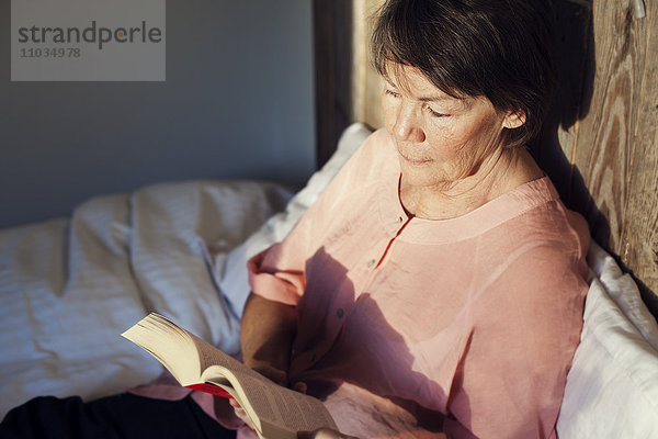 Ältere Frau liest Buch im Bett