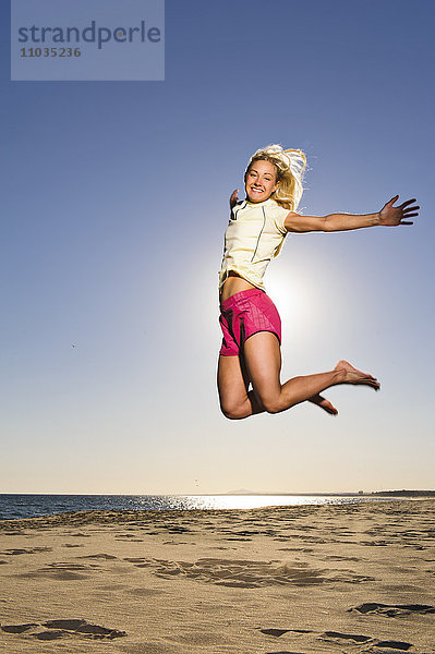 Glückliche junge Frau springt am Strand