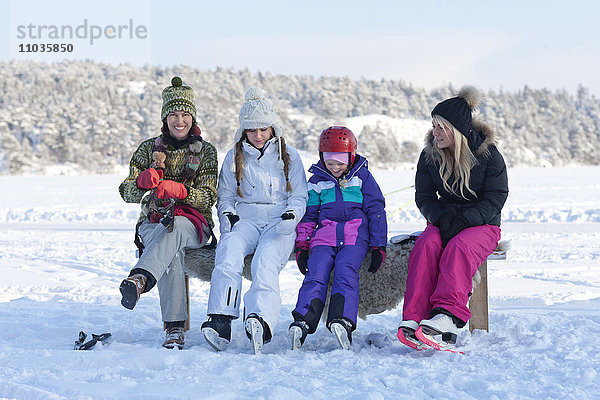 Mutter mit drei Töchtern  die auf einer Bank sitzen und Schlittschuhe anziehen