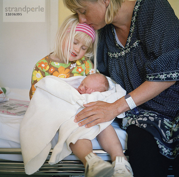 Ein Mädchen mit seinem neugeborenen kleinen Bruder und seiner Mutter  Schweden.
