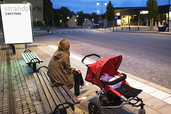 Frau  die auf einer Bank mit einem Kinderwagen wartet  Schweden.