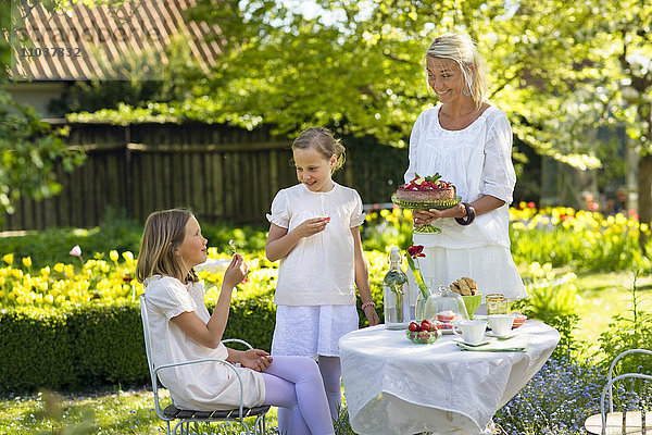 Frau und zwei Mädchen mit einem Erdbeerkuchen in einem Garten  Schweden.