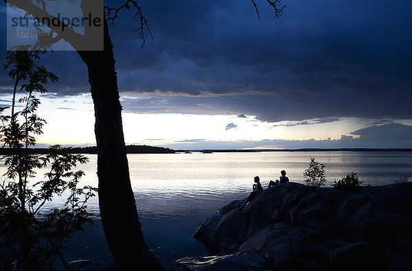 Menschen auf einem Felsen am Meer in der Abenddämmerung  Schweden.