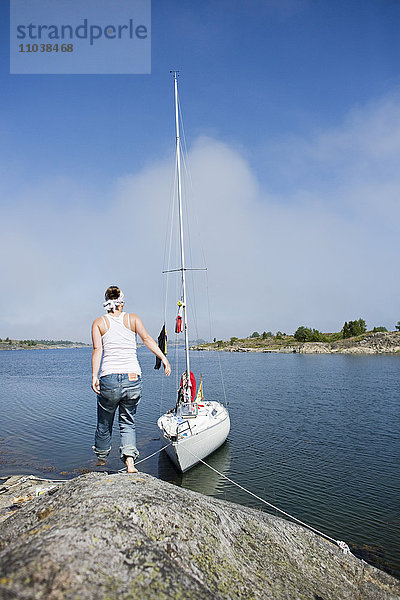 Frau auf einem Felsen neben einem Segelboot  Schweden.