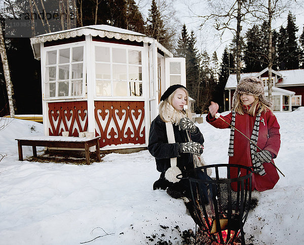 Mädchen grillen Marshmallows vor einem Pavillon
