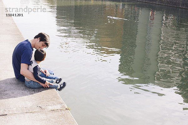 Vater und Sohn am Flussufer sitzend