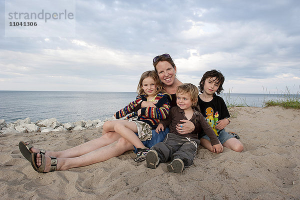 Mutter und Kinder sitzen zusammen am Strand  Portrait