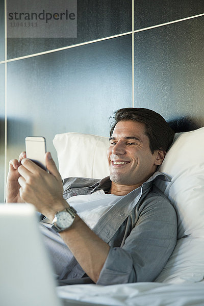 Mann entspannt im Bett mit Multimedia-Smartphone