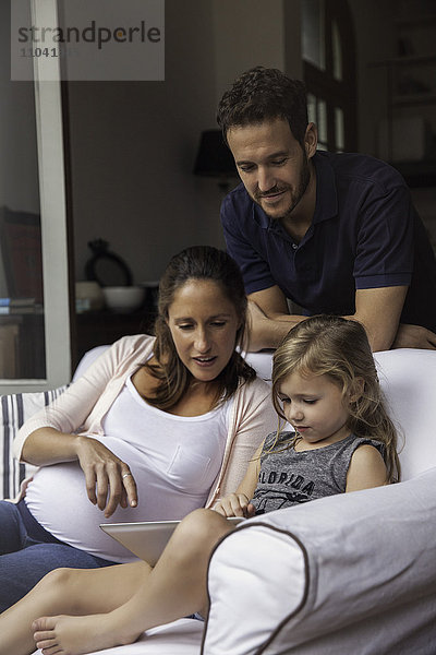 Vater schaut auf als Mutter und Tochter verwenden digitale Tablette zusammen