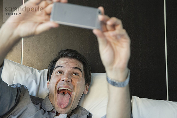 Mann  der ein Smartphone benutzt  um einen Selfie zu nehmen  der die Zunge herausstreckt.