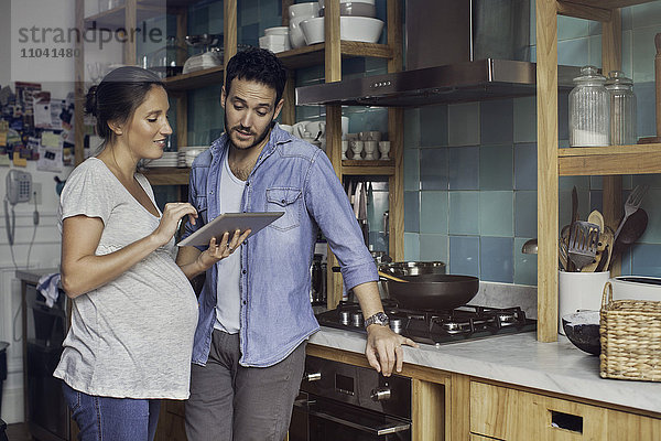 Paar in der Küche mit Blick auf digitales Tablett zusammen