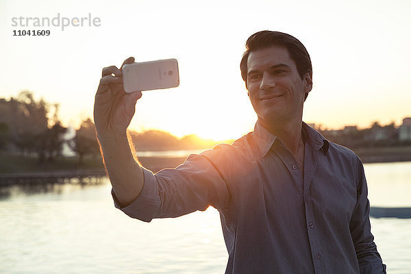 Mann fotografiert sich mit dem Smartphone vor Sonnenuntergang