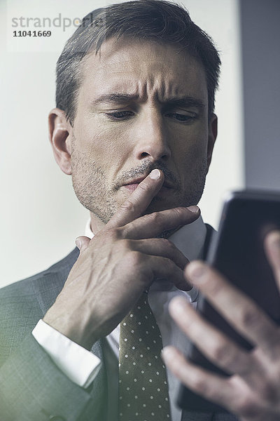 Geschäftsmann betrachtet digitales Tablett mit zerfurchter Stirn