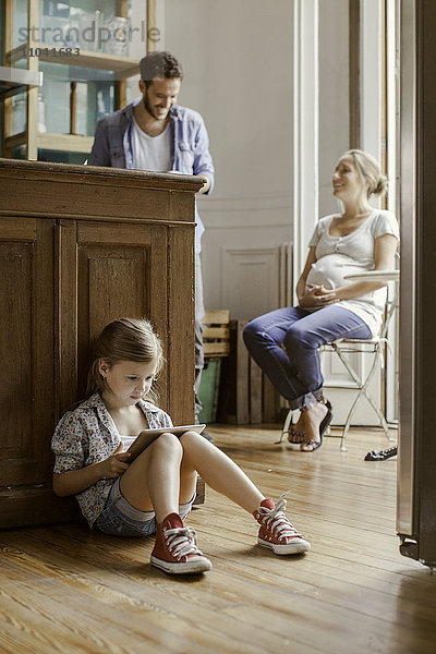 Mädchen sitzt allein und spielt Videospiel  während die Eltern chatten.