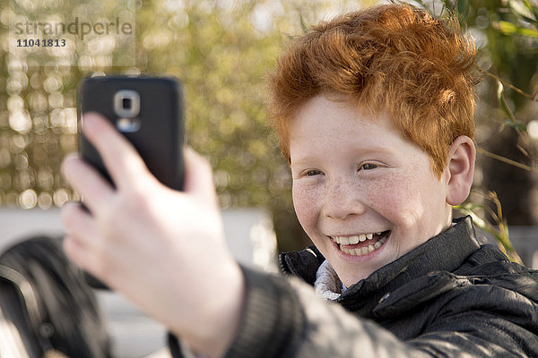 Junge  der ein Smartphone benutzt  um einen Selfie zu nehmen.
