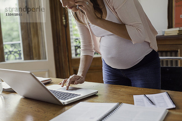 Schwangere Frau mit Laptop-Computer und Telefonieren