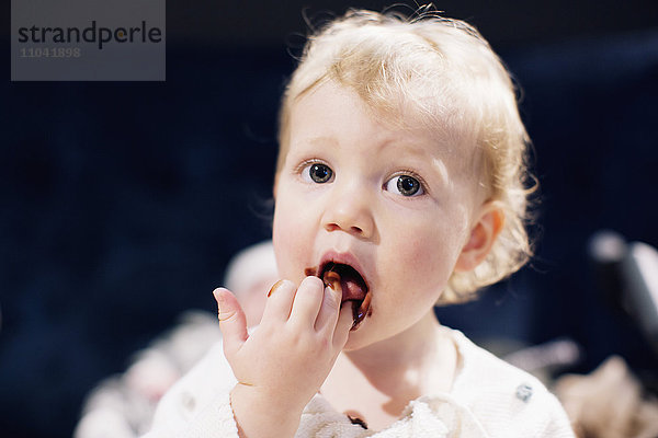 Kleinkind leckt Schokoladensirup von den Fingern