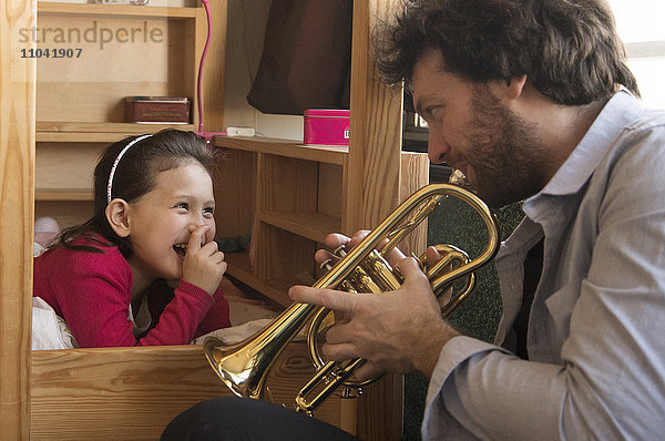 Vater spielt Trompete für kleines Mädchen im Bett liegend
