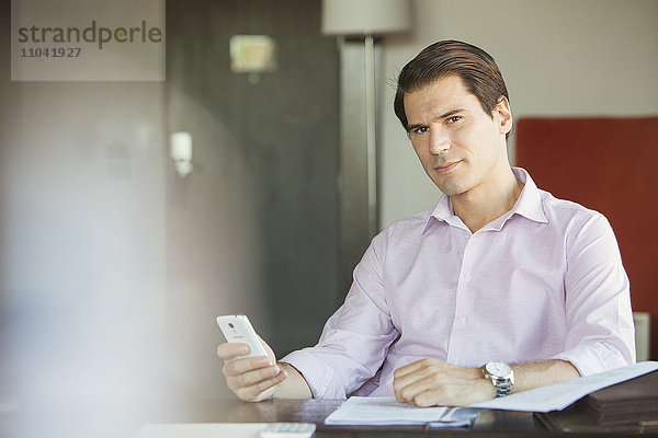 Geschäftsmann mit Smartphone am Schreibtisch  Portrait