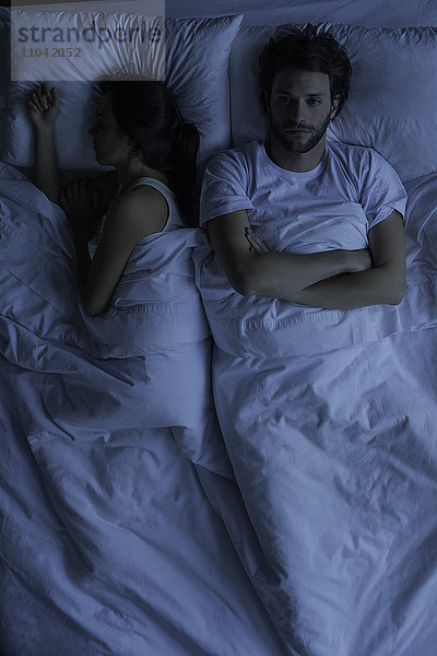 Wach liegender Mann im Bett neben schlafender Frau