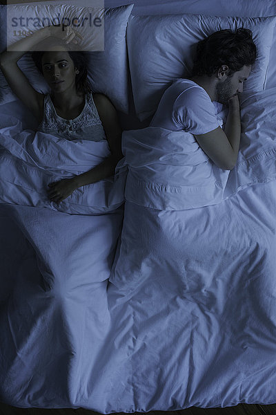 Frau liegt wach neben dem schlafenden Ehemann.
