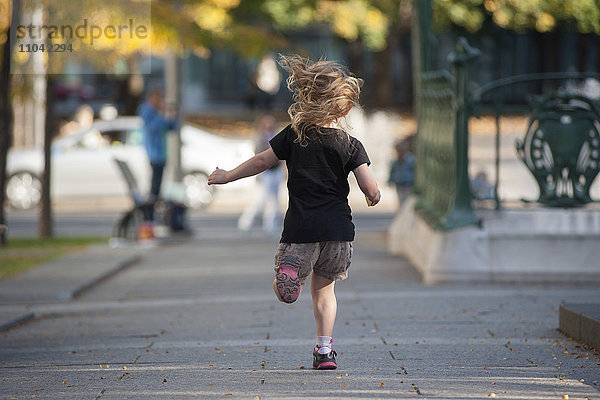 Kleines Mädchen läuft auf dem Bürgersteig